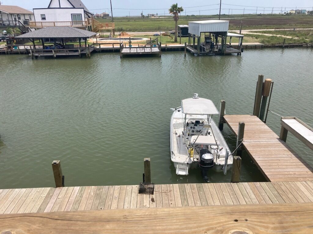 Un barco amarrado en un muelle de madera, con una casa y un área techada al fondo.
