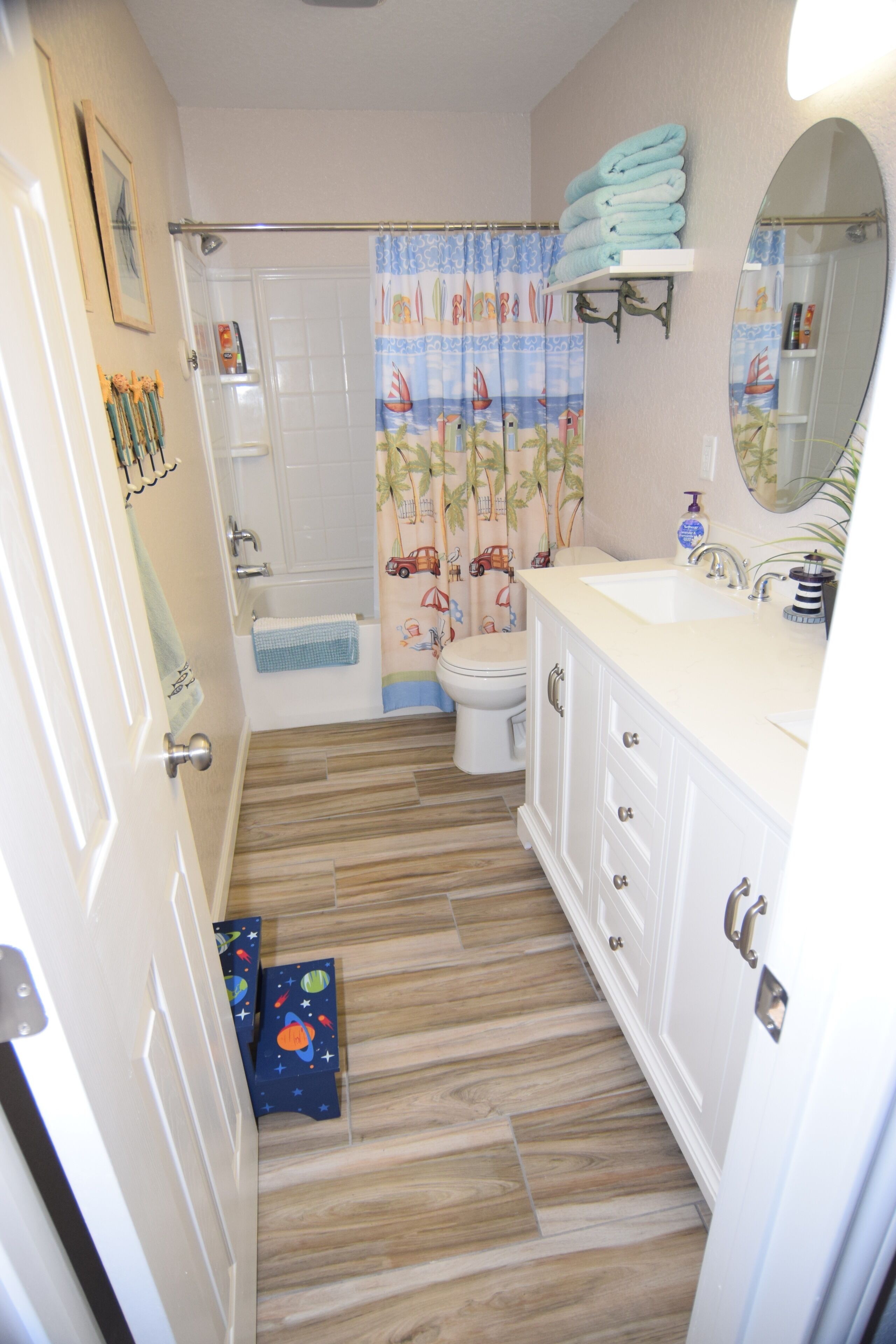 A bathroom with a wooden floor, a toilet, a sink, and a shower curtain with a nautical theme.