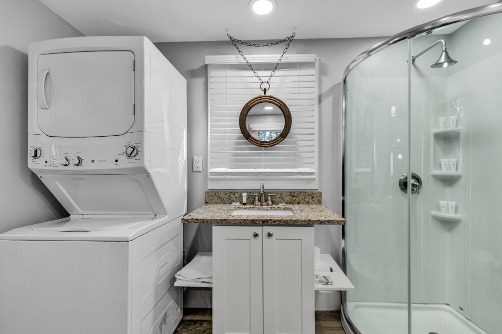 Uma casa de banho compacta com máquina de lavar, lavatório com bancada de granito, espelho e cabine de duche.