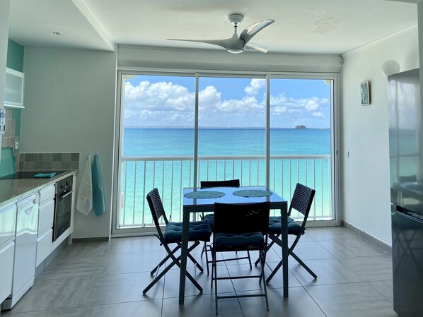 A balcony with a table and chairs, a ceiling fan, and a view of the ocean. - "Blue beach "The best place (grand case)