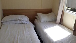 Dos camas individuales con cabeceros de madera, ropa de cama blanca y una ventana con cortinas.