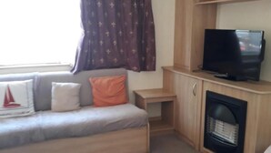 Una sala de estar con sofá, televisión, chimenea y ventana con cortinas.