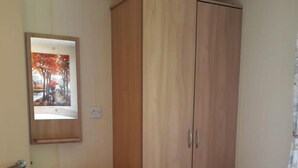 Una habitación con un armario de madera, un espejo y un enchufe en la pared.