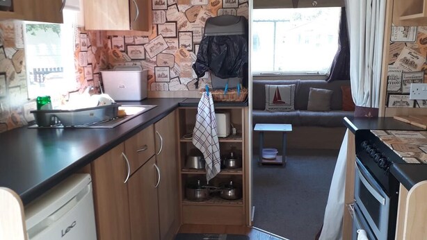 Cocina compacta para autocaravana con armarios de madera, estufa integrada y zona de comedor con ventana.