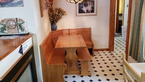 Un coin repas avec un banc et une table en bois, une horloge décorative et une étagère murale remplie de livres.