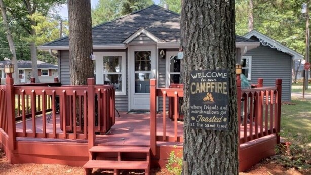 Un chalet avec foyer extérieur, doté d’une rambarde rouge et d’un escalier en bois menant à l’entrée.