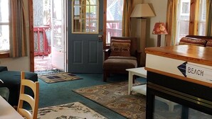 Une pièce chaleureuse avec une porte bleue, une table en bois sur laquelle est posé un panneau indiquant « PLAGE », une chaise, une lampe et une vue sur l’extérieur.