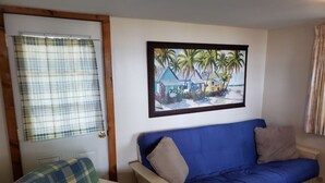 A room with a blue sofa, a plaid armchair, and a painting of palm trees on the wall.