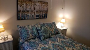 A bedroom with a bed, two bedside tables with lamps, a ceiling fan, and a wall-mounted painting.