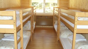 Una habitación con cuatro literas en fila, paredes de madera y una ventana con persianas.
