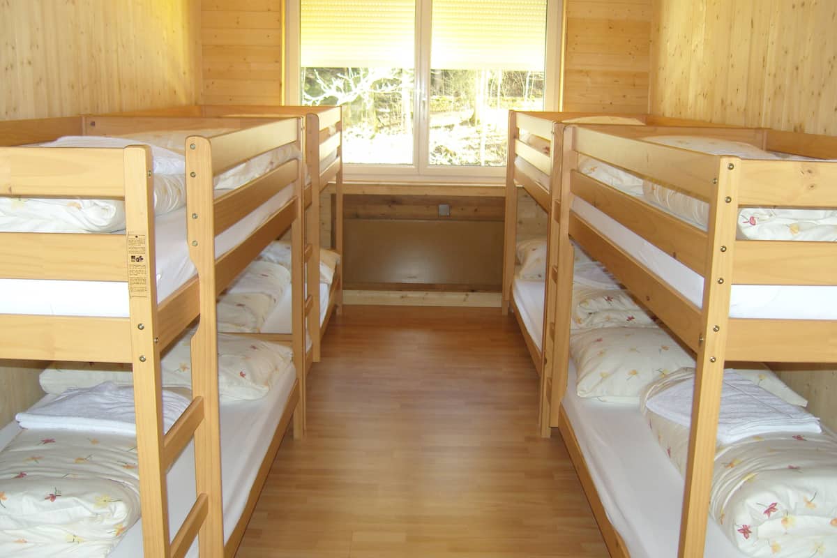 A room with four bunk beds aligned in a row, wooden walls, and a window with blinds.