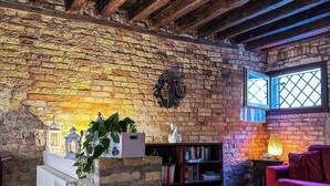 Un salon rustique avec des poutres apparentes, un mur en briques, une bibliothèque, un canapé rouge et un tapis à motifs.