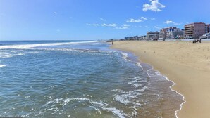 Een strand met een zandstrand en een helderblauwe lucht. Er staan gebouwen op de achtergrond.
