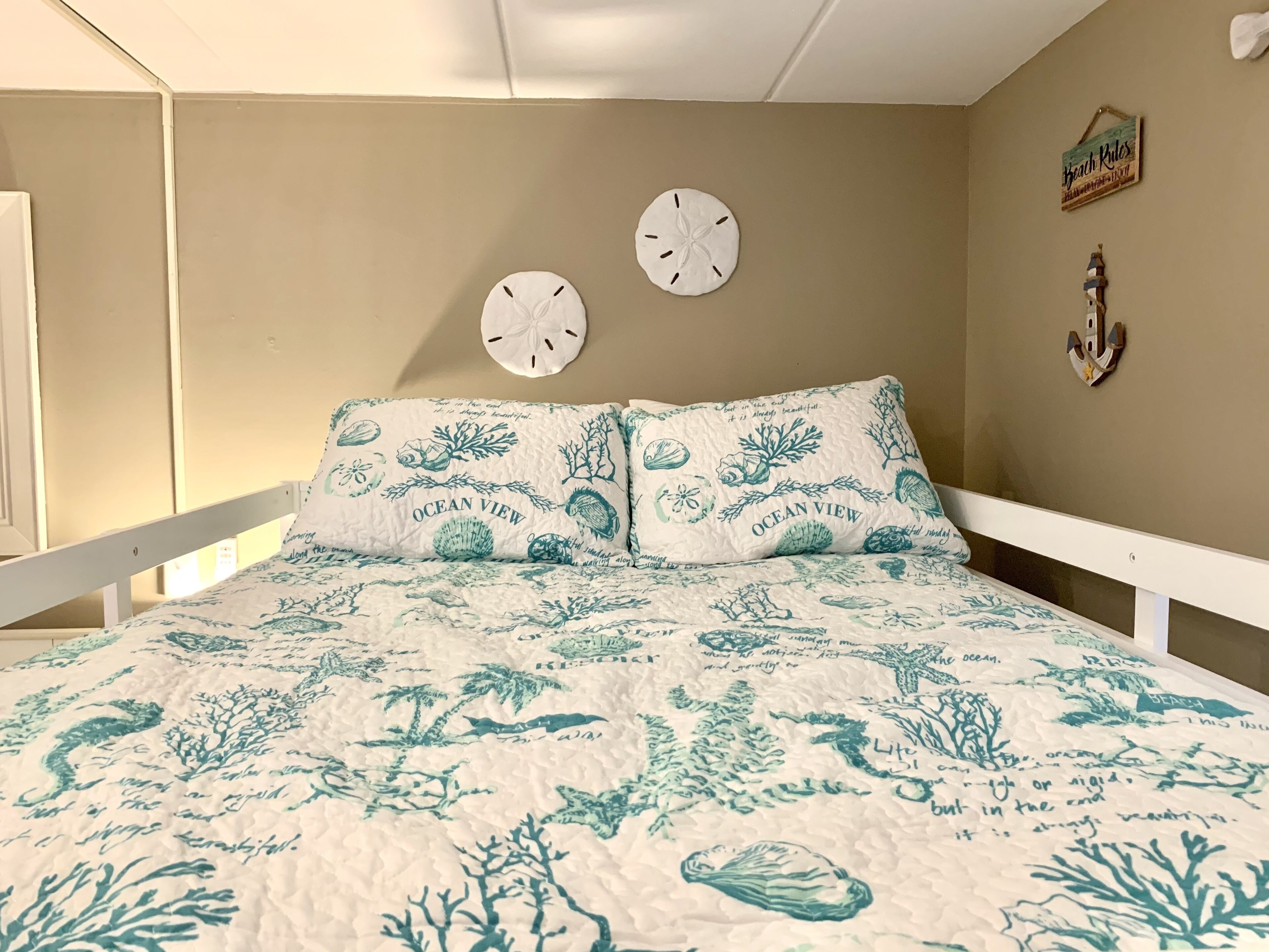 A bedroom with a bed featuring a beach-themed quilt and matching pillows, a white headboard, and a wall clock.