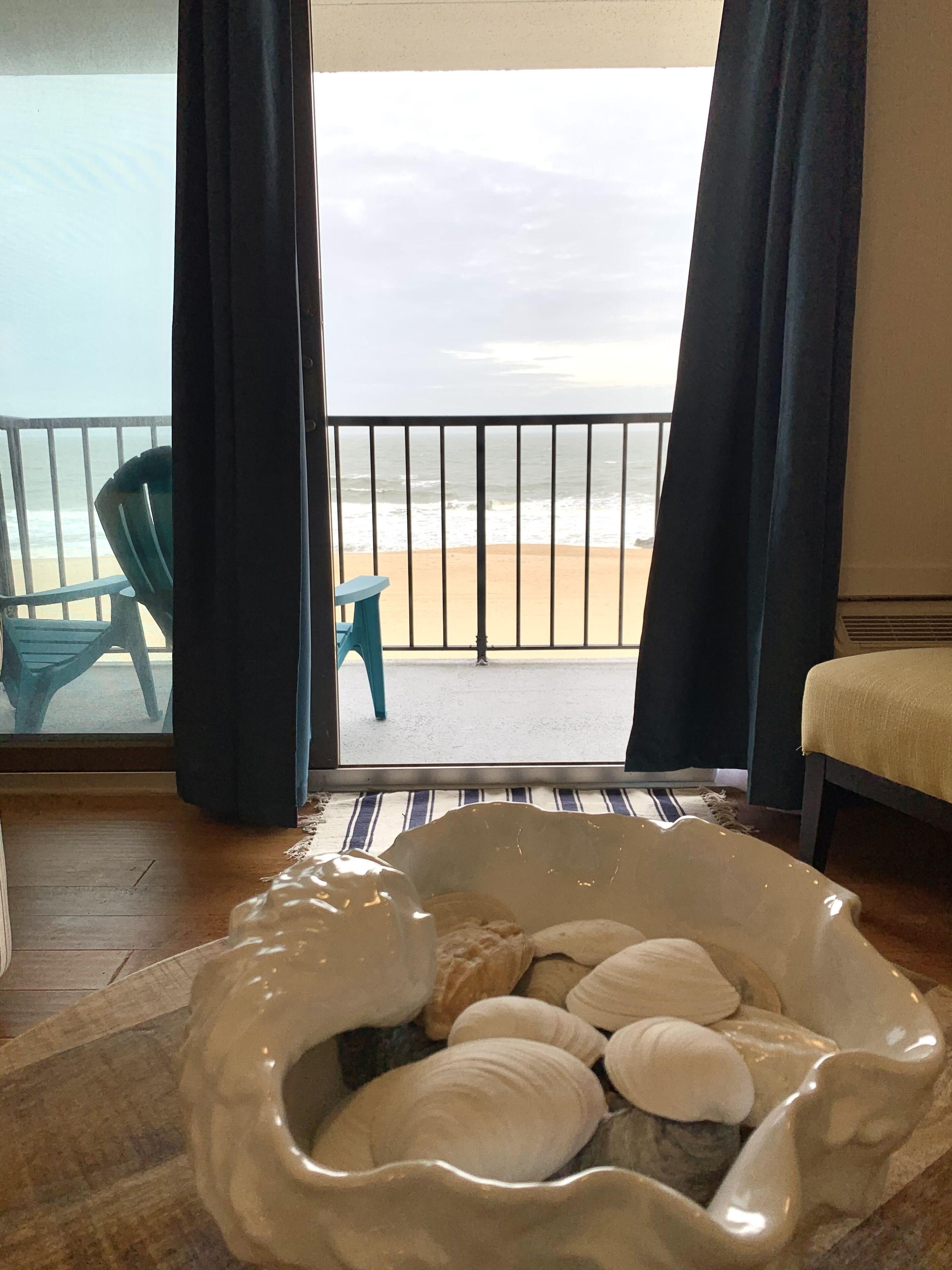 Une pièce avec vue sur la plage, une chaise bleue, une petite table et un bol décoratif blanc agrémenté de coussins.