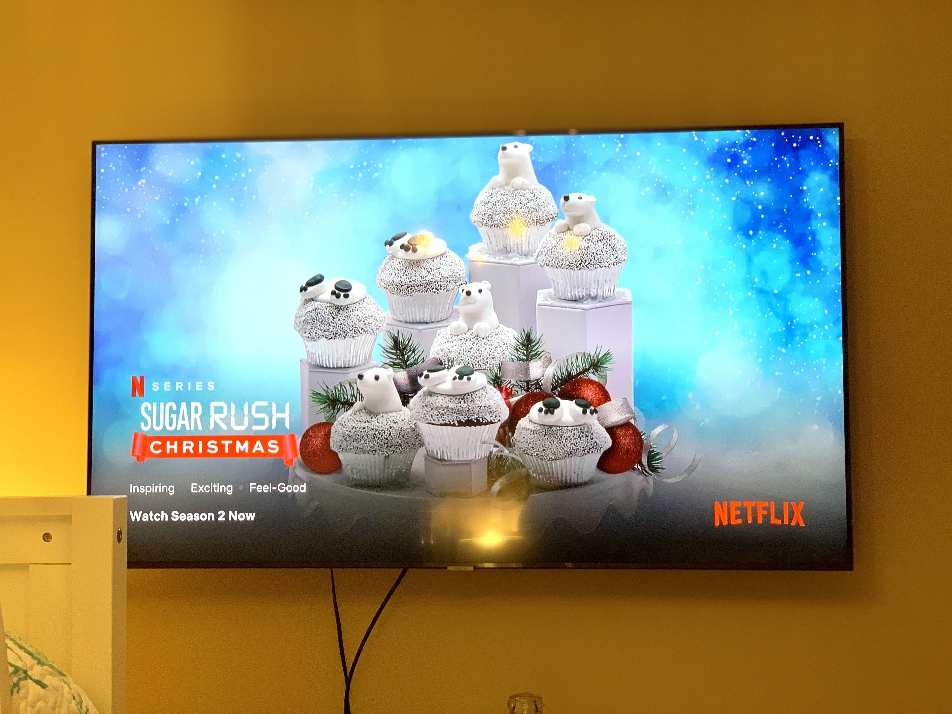 A television displaying a Christmas-themed Netflix series advertisement with a snowy scene and cupcakes.