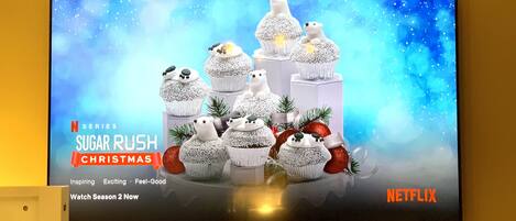 A television displaying a Christmas-themed Netflix series advertisement with a snowy scene and cupcakes.