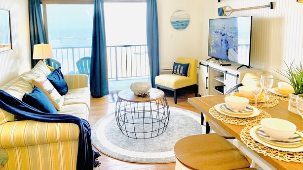Een goed verlichte woonkamer met een bank, fauteuil, eettafel en televisie.