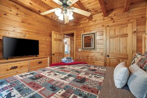 Quarto de cabana de madeira com uma cama grande, televisão e ventilador de teto.