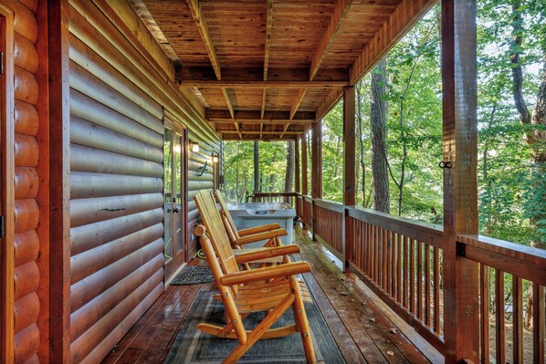 A wooden cabin with a porch featuring rocking chairs and a view of the forest.