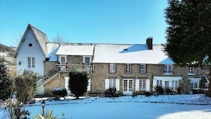 Een gebouw van steen met een witte gevel, een grote schoorsteen en een erf bedekt met sneeuw.
