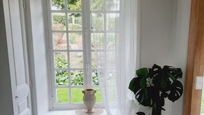 Een kamer met een groot raam, een radiator, een kamerplant en een vloer met een honingraatpatroon.