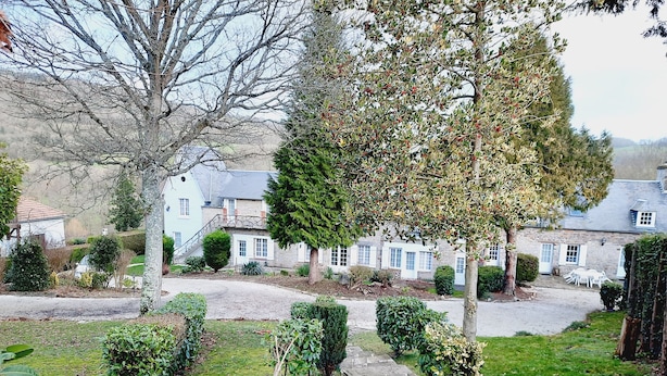 Een stenen pad dat leidt naar een rij traditionele stenen huizen, met een verzorgde tuin en een grote boom op de voorgrond.
