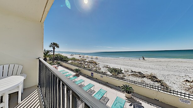 A balcony with a view of a beach, lounge chairs, and a palm tree. - 🌊 Kima 103 — Gulf Front 2BR Condo with Panoramic Views & Private Balcony (Madeira Beach)