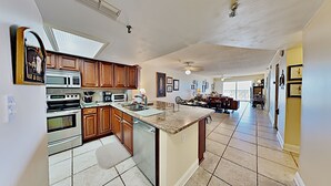 A spacious kitchen with wooden cabinets, a large island, and a dining area with a sofa and chairs. - 🌊 Kima 103 — Gulf Front 2BR Condo with Panoramic Views & Private Balcony (Madeira Beach)