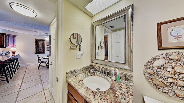 A bathroom with a granite countertop, a sink, a large mirror, and a decorative wall piece. - 🌊 Kima 103 — Gulf Front 2BR Condo with Panoramic Views & Private Balcony (Madeira Beach)