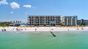 A beachfront hotel with multiple floors, a sandy beach, and umbrellas. - 🌊 Kima 103 — Gulf Front 2BR Condo with Panoramic Views & Private Balcony (Madeira Beach)