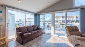 En rummelig opholdsstue med en brun sofa og en lænestol, store skydedøre der fører ud til en terrasse med pool og udsigt over et boligområde.