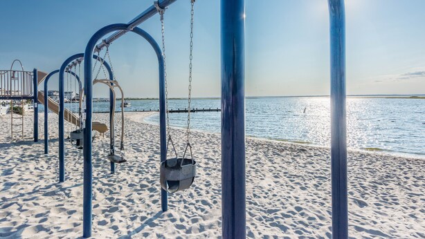 En strandlegeplads med gynger og rutchebane med udsigt over et roligt hav.