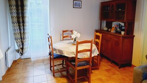 Uma sala de jantar com uma mesa posta para dois, cadeiras de madeira, um armário com portas de vidro e uma janela com cortinas.