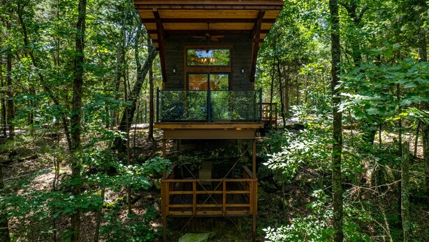 Una casa en el árbol de madera con balcón, rodeada de un bosque frondoso.
