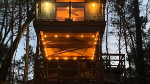 Una cabaña de madera de dos pisos con balcón y luces colgantes.