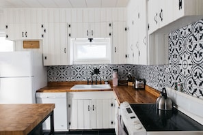 A kitchen with white cabinets, a wooden countertop, a sink, a stove, and a window.