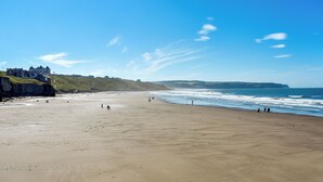 Ein weiter, sandiger Strand mit einigen Personen, die dort entlanggehen und stehen, mit Blick auf den Ozean.