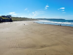 A wide sandy beach with a few people walking and standing, overlooking the ocean. - Seaton Cottage - UK31990 (Staithes)