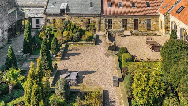 Ein Innenhof mit Steingebäuden, Kiesflächen und ordentlich geschnittenen Hecken.