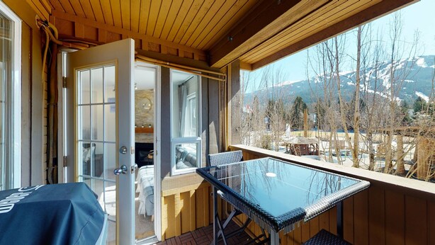 Un balcón con mesa y sillas de vidrio, techo de madera y vistas a un paisaje montañoso.