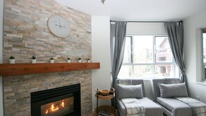 Un salón acogedor con chimenea de piedra, un conjunto de sofás y un ventanal con cortinas.