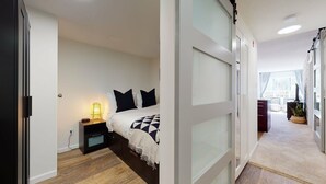 Un dormitorio moderno con cama, mesita de noche, lámpara y vistas a un salón.