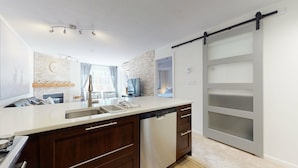 Una cocina moderna con lavavajillas, un lavamanos y una puerta corredera que da a un dormitorio.
