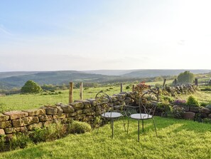 A stone wall with a metal table and chairs in a grassy field with a view of rolling hills. - A cosy little cottage, full of character, history and charm. (Egton)