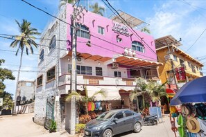 Ein mehrstöckiges Gebäude mit rosa Fassade, ein Geschäft im Erdgeschoss und ein geparktes Auto.