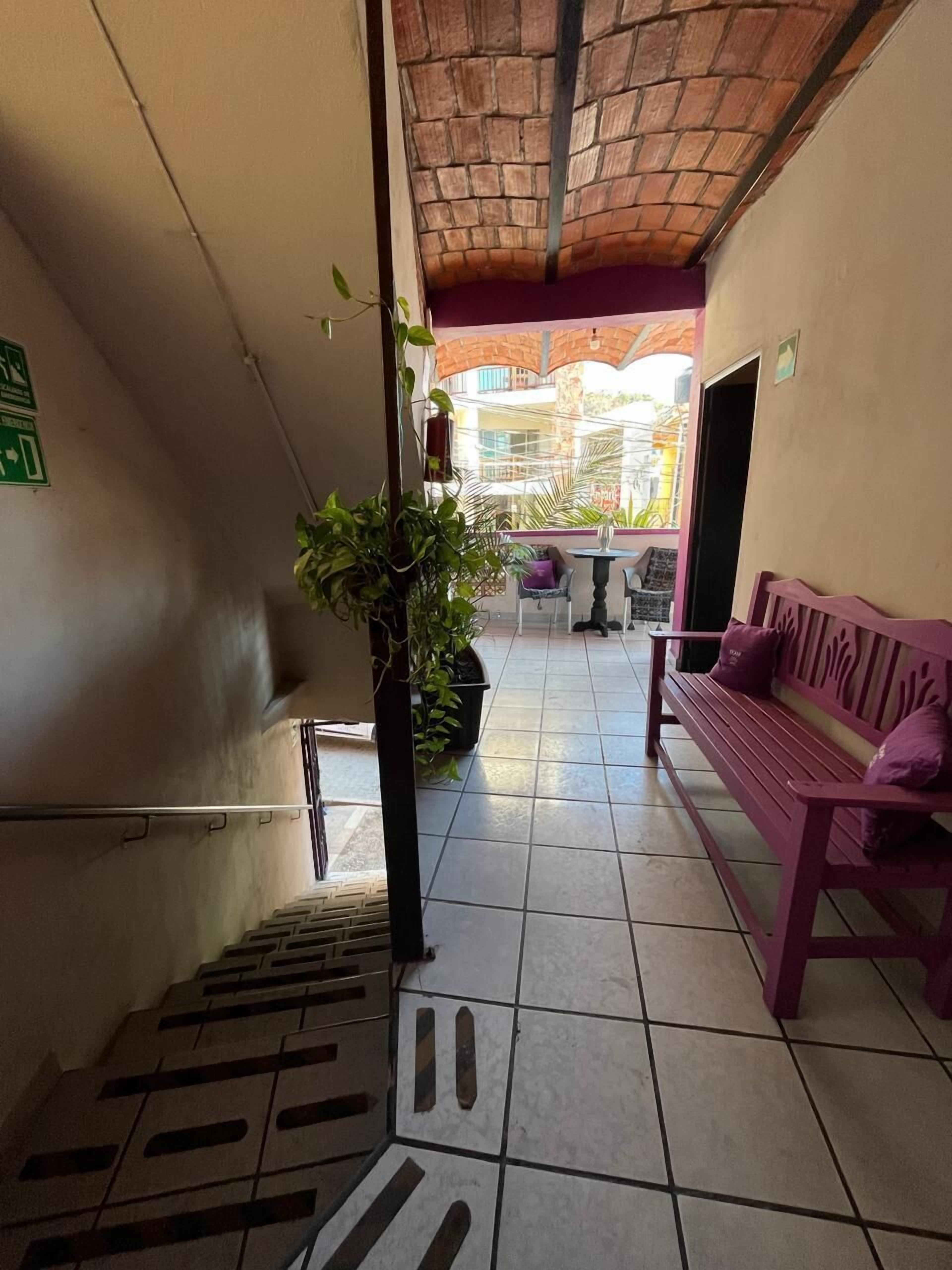 Un pasillo con suelo de baldosas, una escalera, un banco y una planta en maceta.