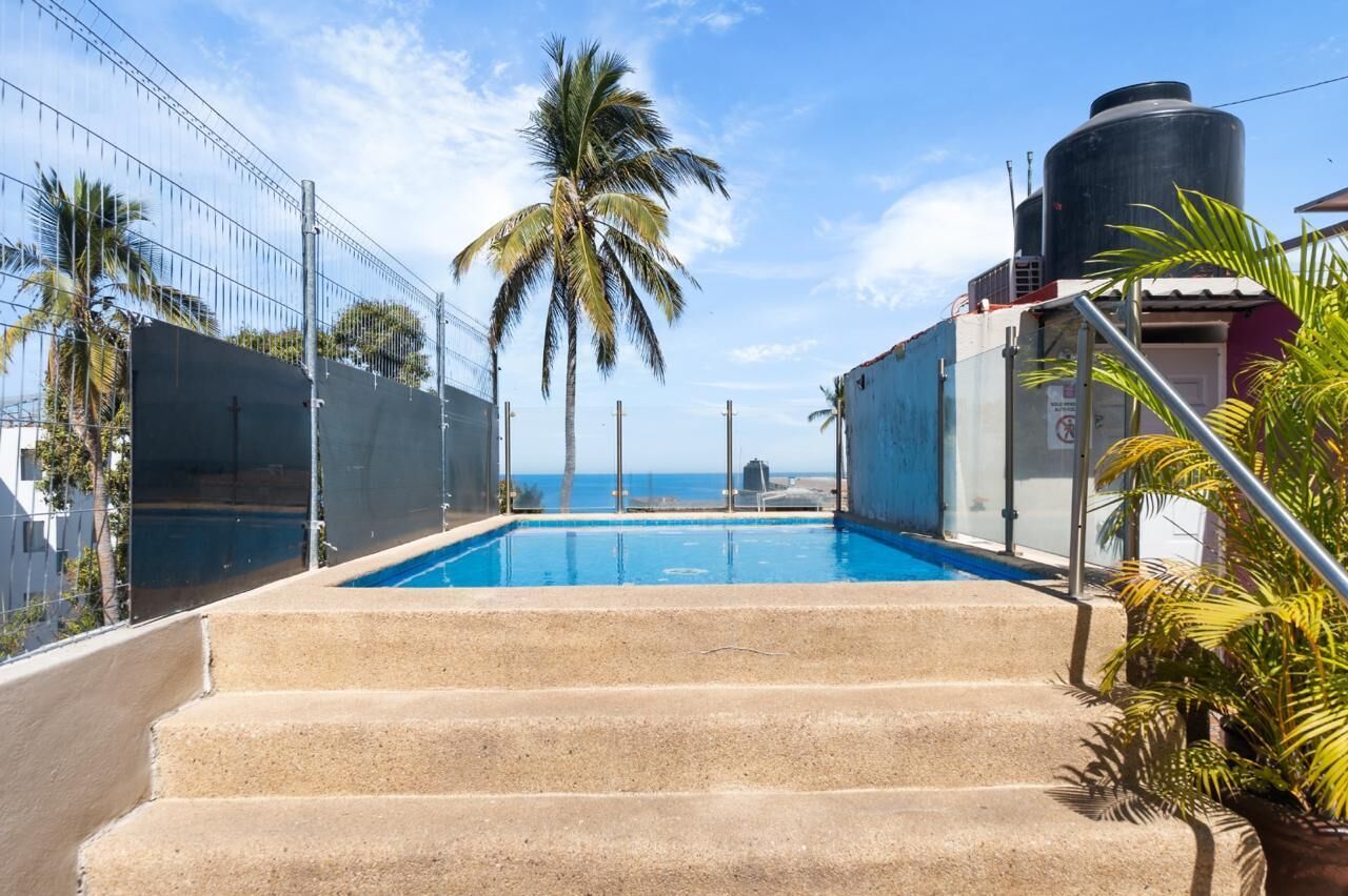 Une piscine accessible par des marches, entourée d’une clôture et de palmiers.