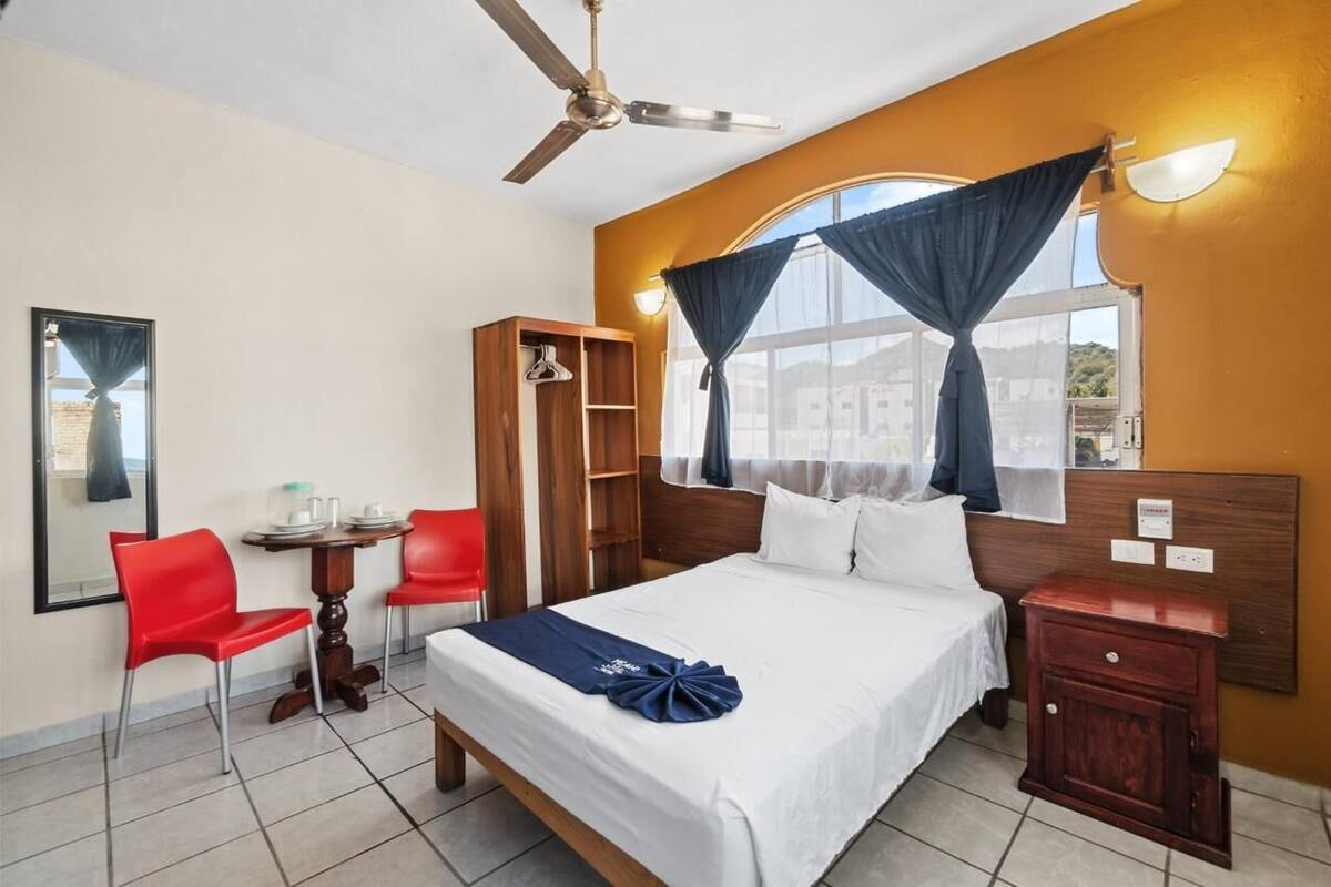 Una habitación de hotel con cama, escritorio con silla, armario y ventana con cortinas.
