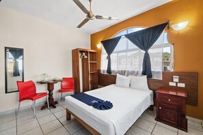 Ein Hotelzimmer mit Bett, Schreibtisch mit Stuhl, Kleiderschrank und einem Fenster mit Vorhängen.